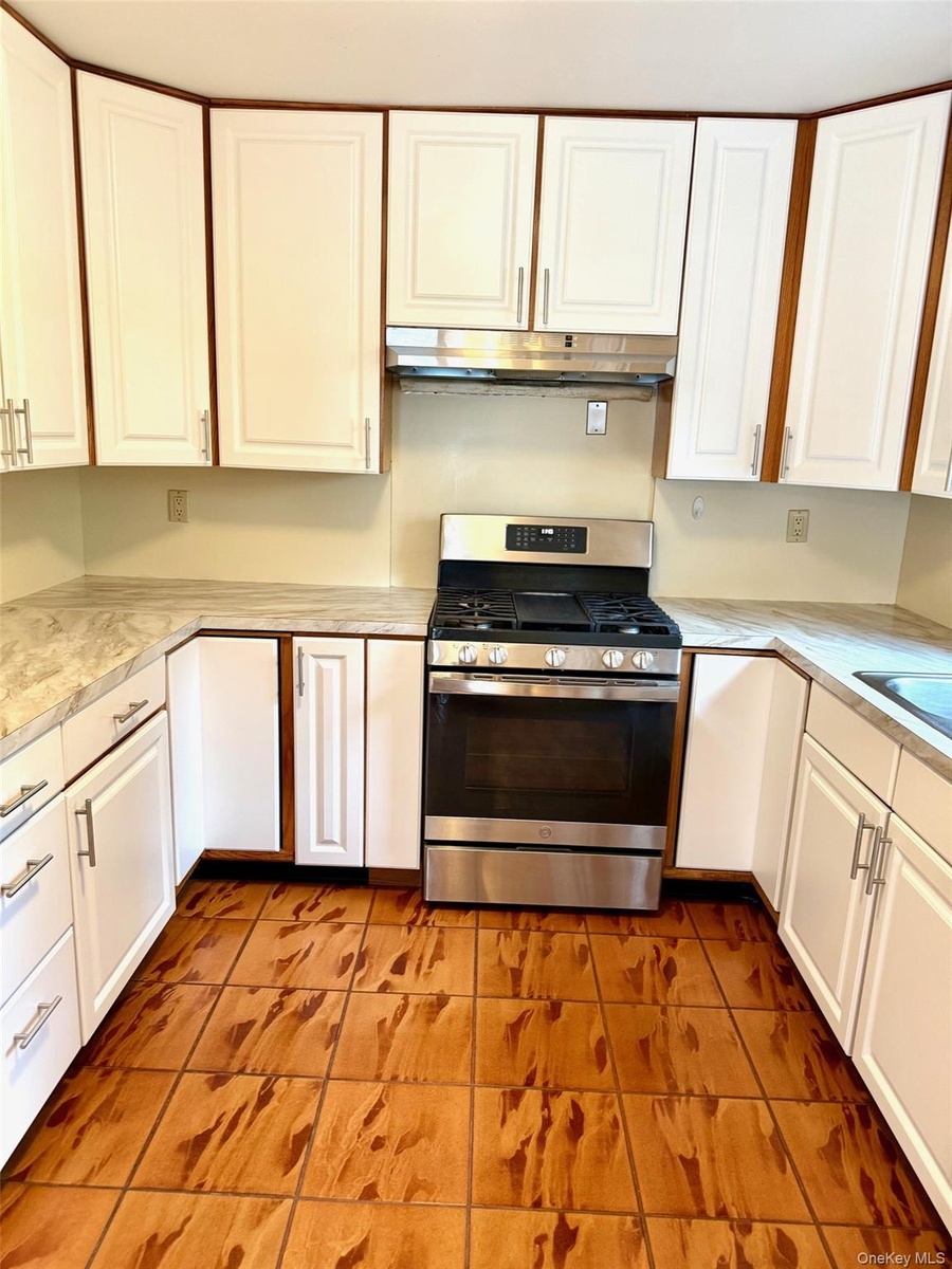 Kitchen with stainless steel gas range, white cabinets, light tile patterned floors, and light countertops
