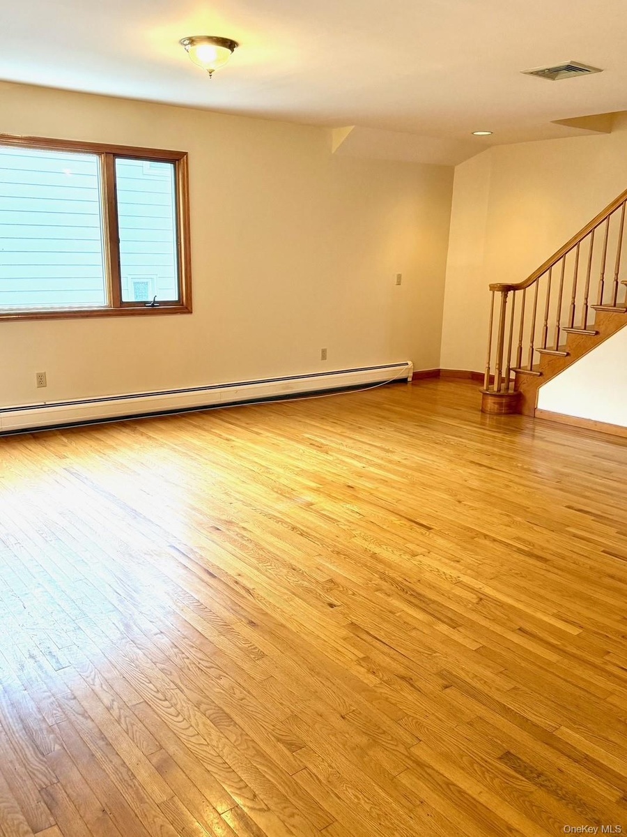 Empty room with light wood-style flooring, stairway, and a baseboard radiator