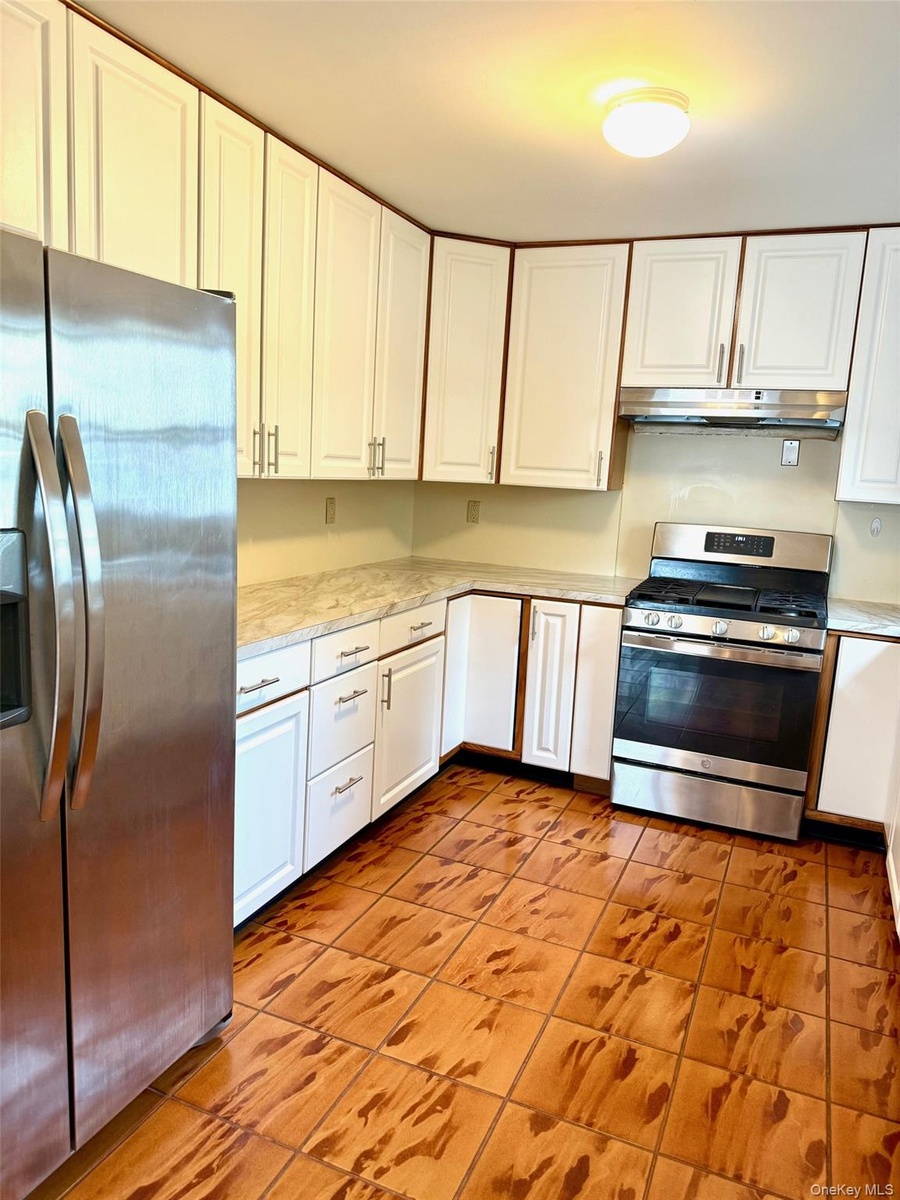Kitchen featuring appliances with stainless steel finishes, white cabinetry, light tile patterned floors, and under cabinet range hood