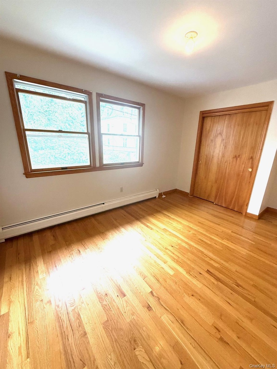 Unfurnished bedroom with a baseboard radiator, light wood-style flooring, and a closet