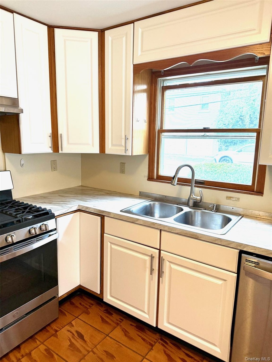 Kitchen featuring stainless steel appliances, white cabinets, light countertops, dark tile patterned floors, and under cabinet range hood