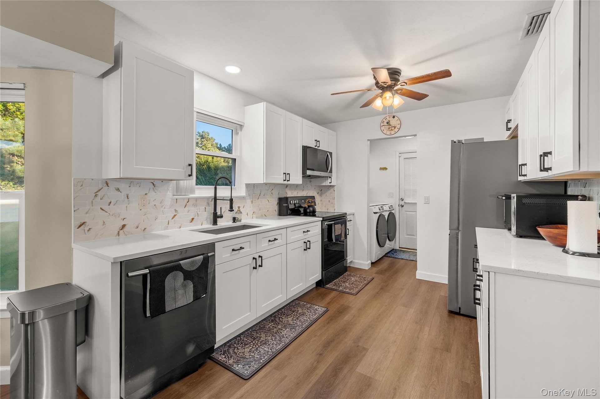 Kitchen featuring white shaker cabinetry, white quartz countertops, a decorative tile backsplash, stainless steel appliances, and wood-finish flooring