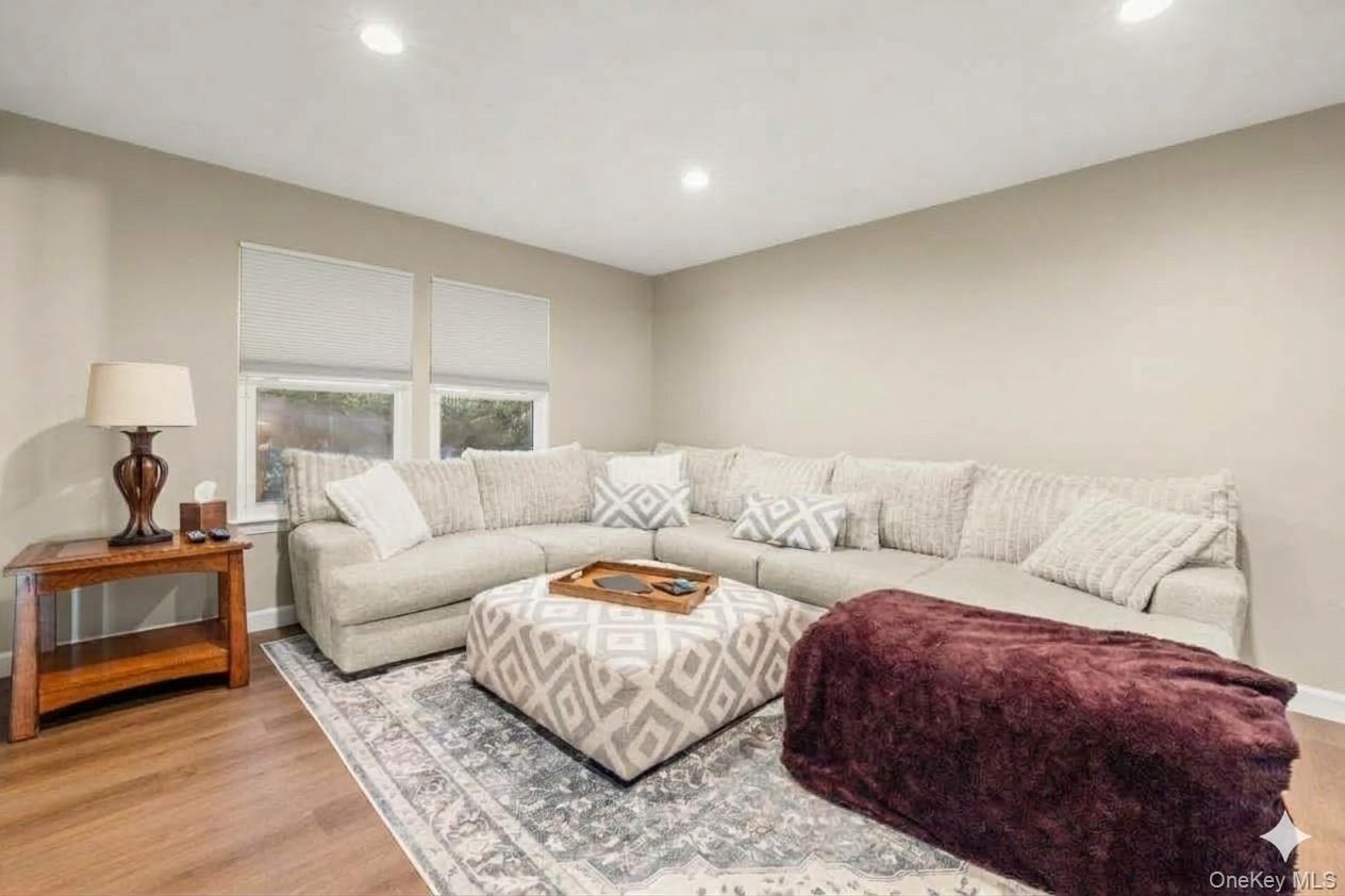 SPACIOUS Living Room. Recessed lighting, wood-finish flooring, two windows with roller shades, and light-toned walls., AI edited.