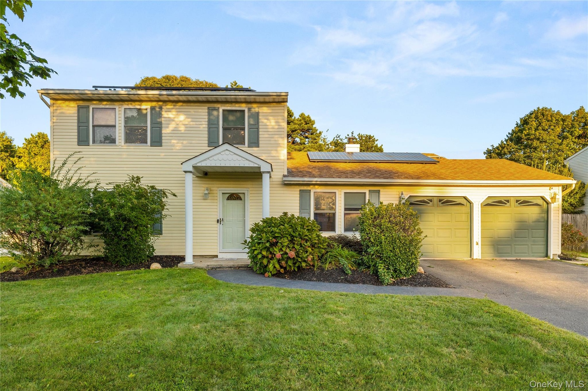 Two-story residence featuring light-toned siding, a covered entryway, an oversized driveway and a two-car garage with arched panel doors
