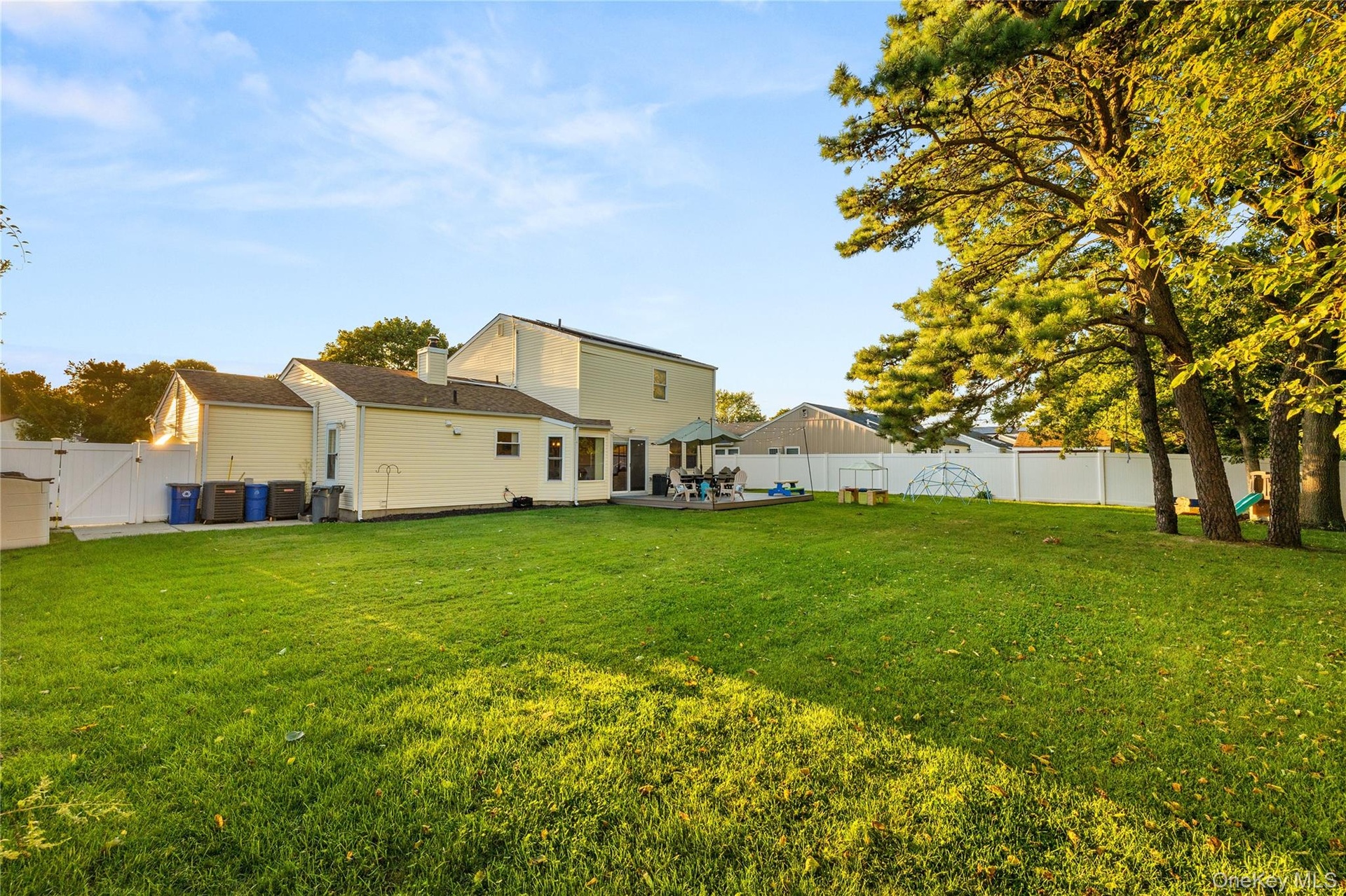 Expansive backyard featuring a manicured lawn, mature trees, and a white privacy fence