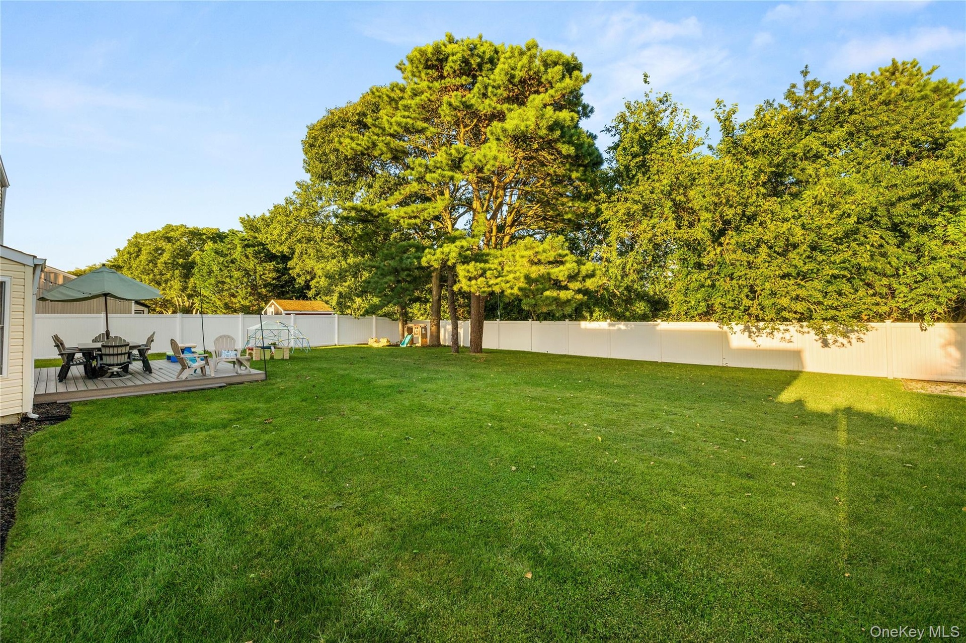 Expansive backyard featuring a manicured lawn, established trees, a raised deck, and a white privacy fence