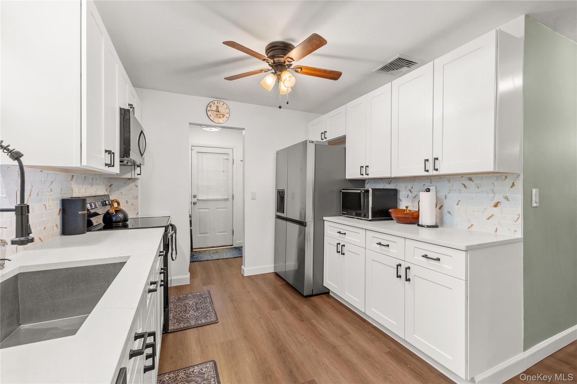 Kitchen featuring white shaker-style cabinetry, stainless steel appliances, wood-finish flooring, and light-toned countertops
