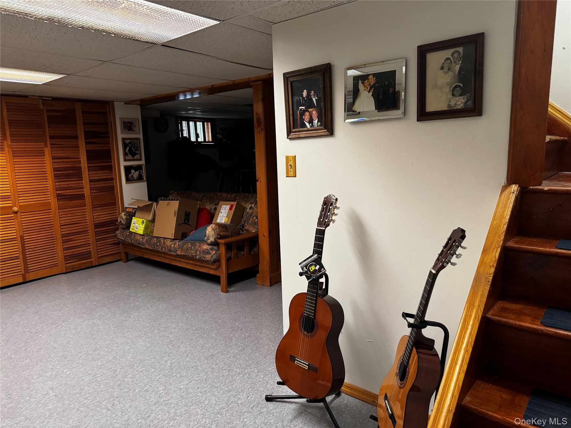 Wood slat bi-fold closet doors, drop ceiling with fluorescent lighting, wood staircase, and wood door frame