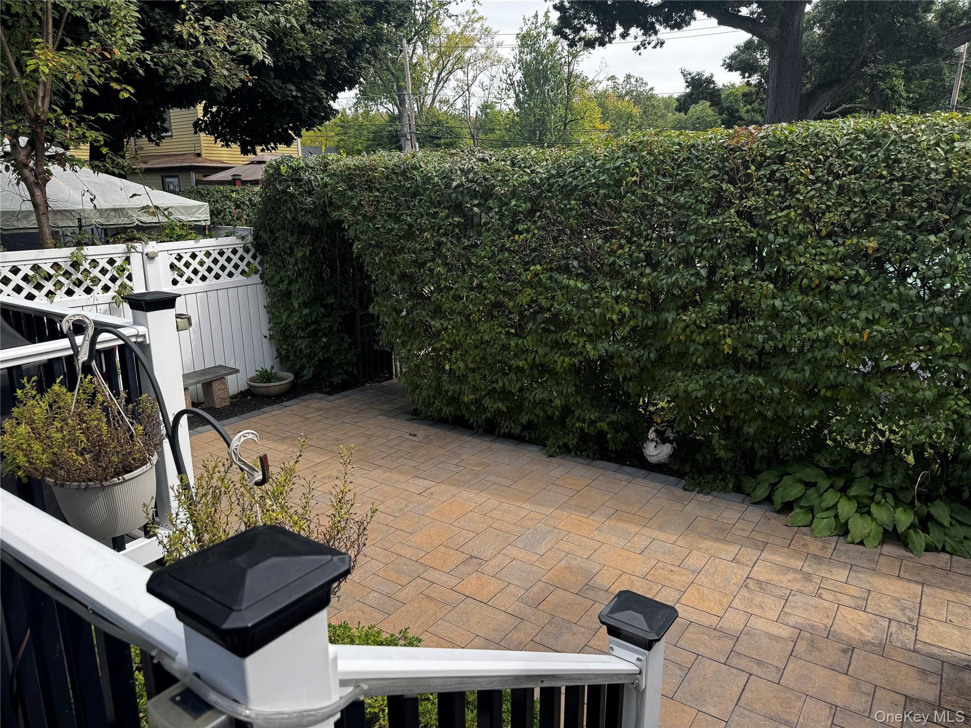 Paver patio with a tall privacy hedge and lattice fencing
