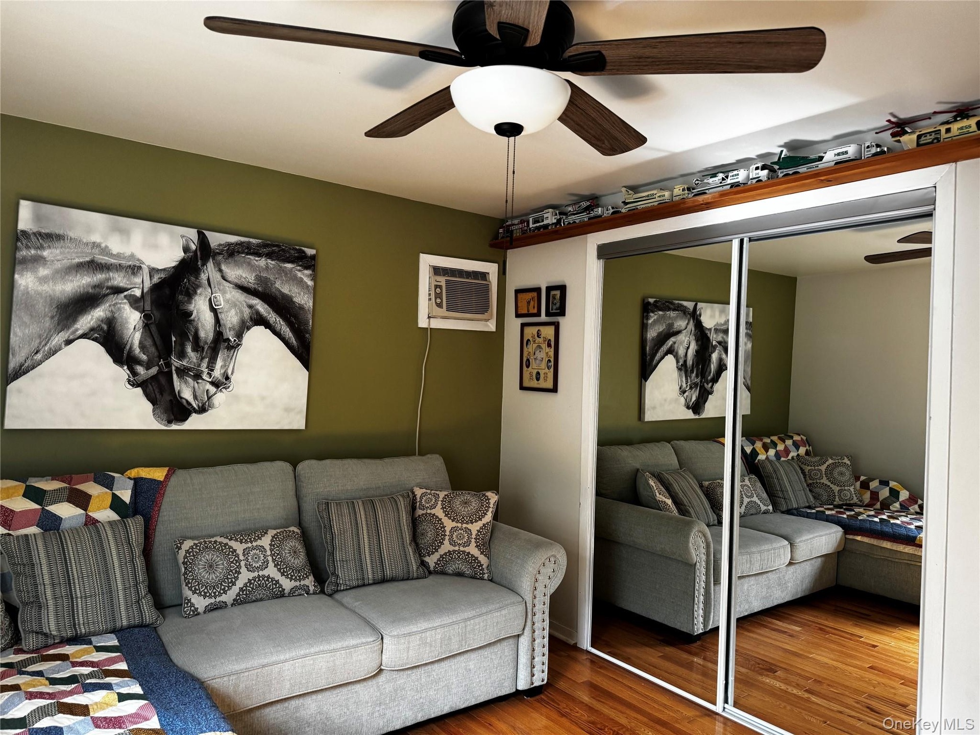 Wood-finish flooring, ceiling fan with light fixture, mirrored closet doors, and a built-in air conditioning unit