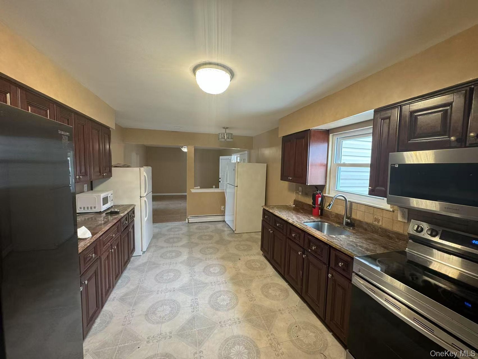 Kitchen featuring decorative backsplash, stainless steel appliances, dark brown cabinets, a sink, and a baseboard heating unit