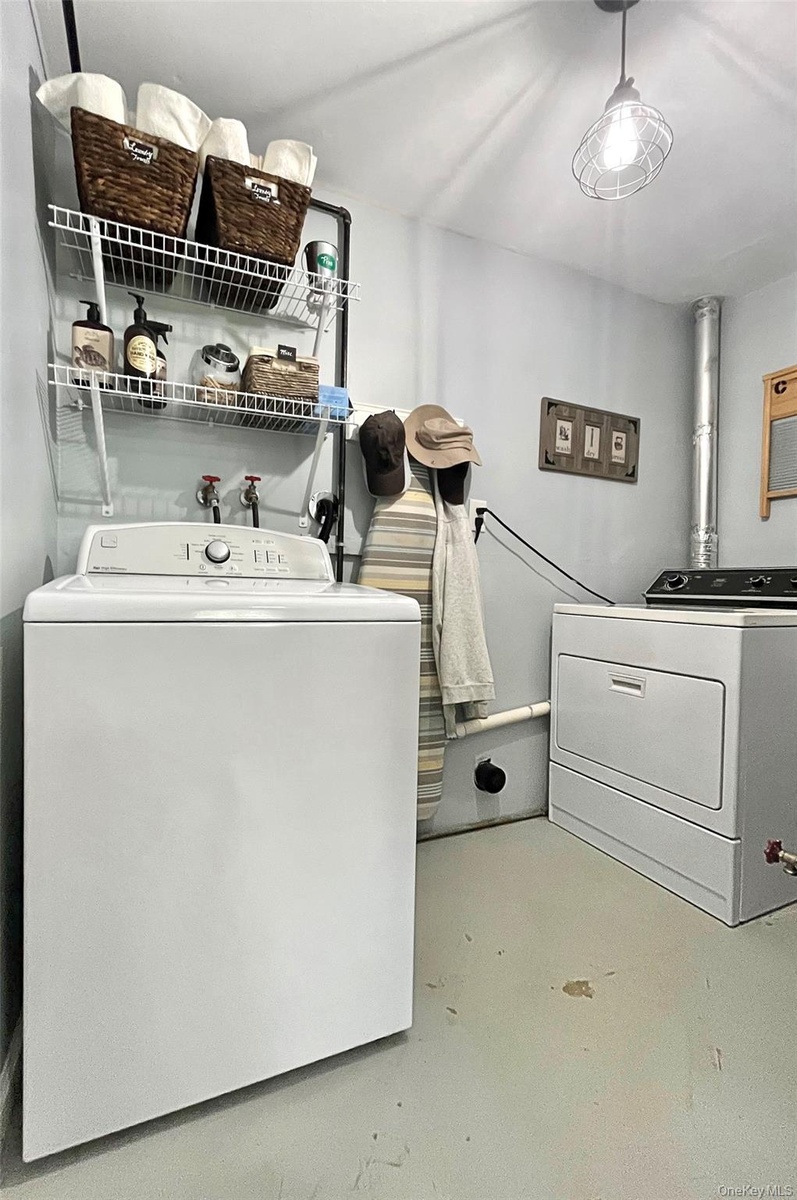 Laundry area with painted concrete flooring, two wall-mounted wire shelving units, and a ceiling-mounted caged light fixture