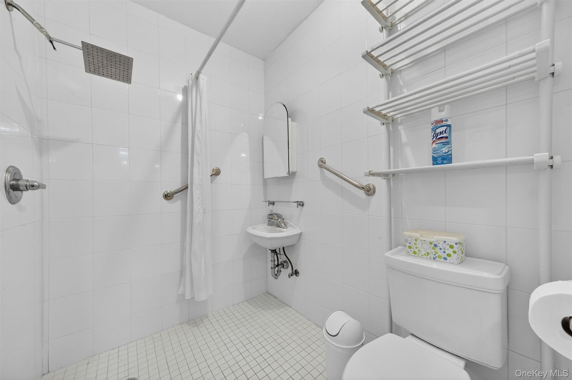 White tiled shower with a rain-style showerhead, wall-mounted grab bars, and a white shower curtain