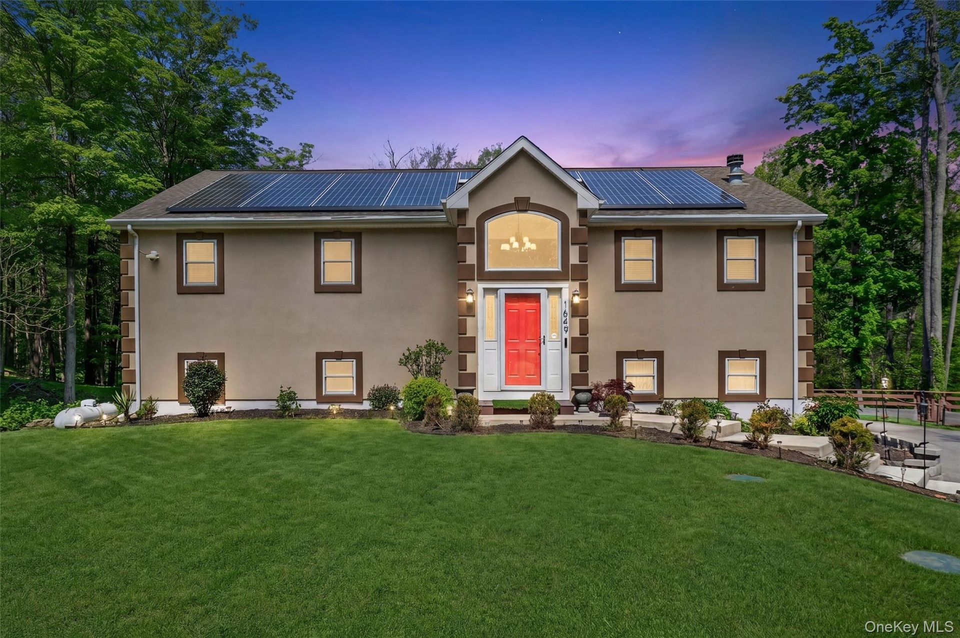 Stucco exterior with stone-look corner accents, solar panel array, arched entry window, red front door, and established landscaping