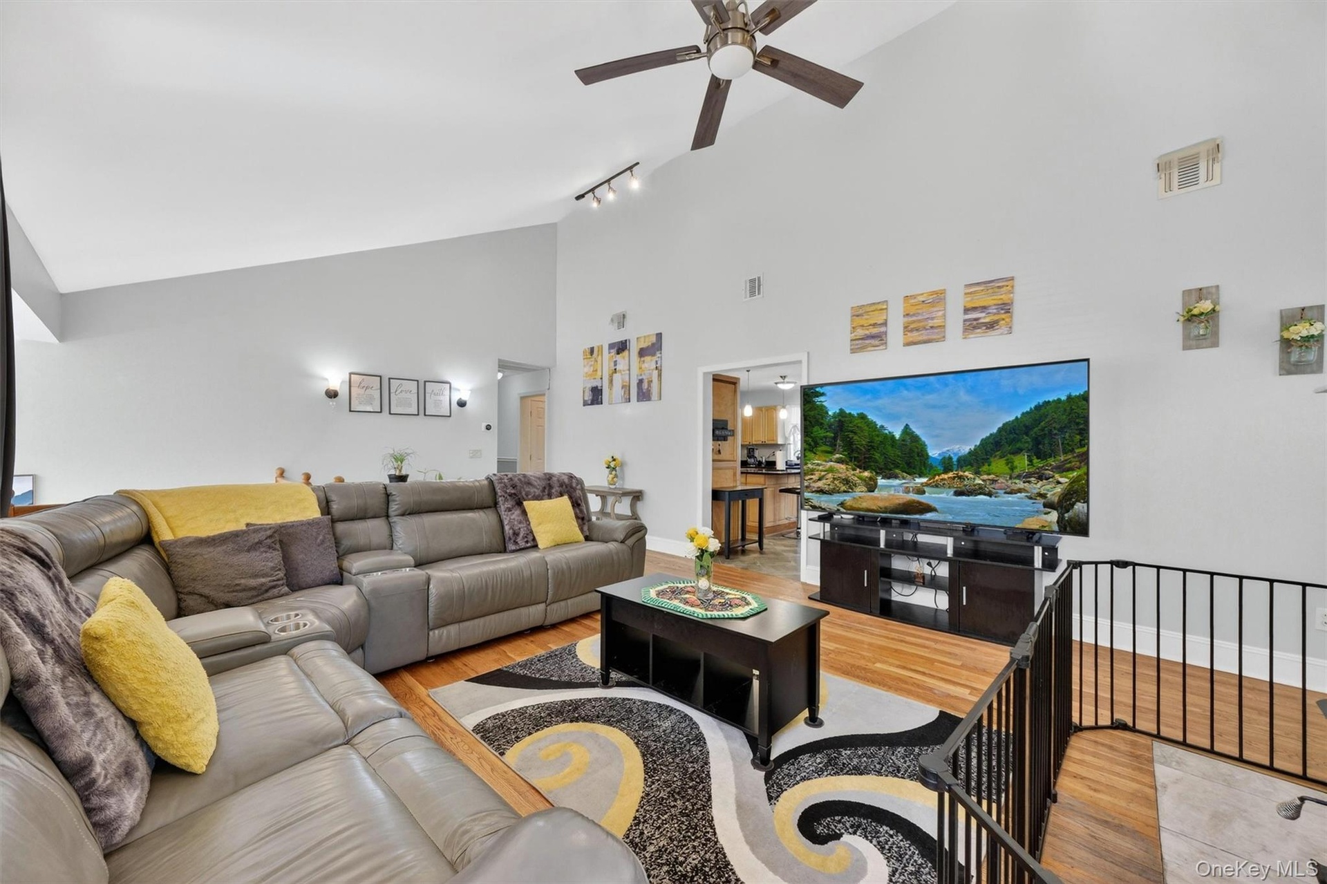 Vaulted ceilings with a ceiling fan, track lighting, wood-finish flooring, and a black metal railing