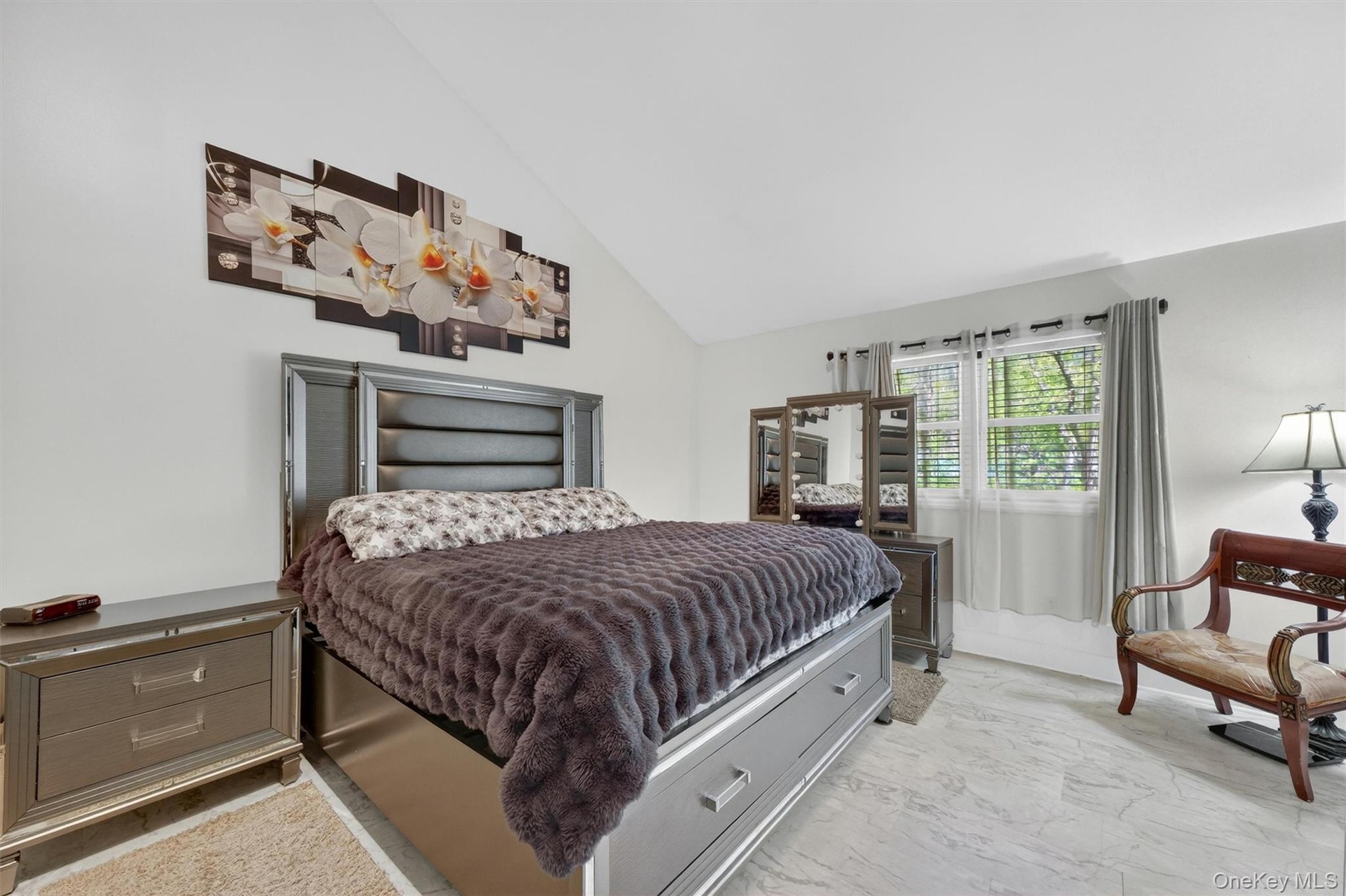 Vaulted ceiling, window with blinds and drapes, light-toned flooring, and built-in dresser with mirror