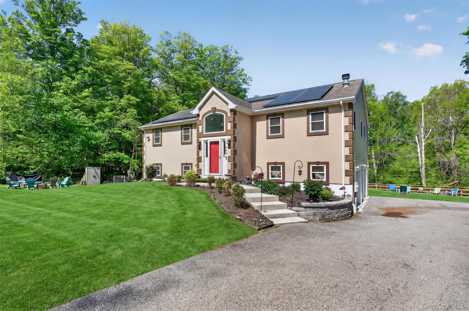 Stucco exterior with stone-look accents, prominent red front door, multiple windows, solar panels on roof, and a paved driveway