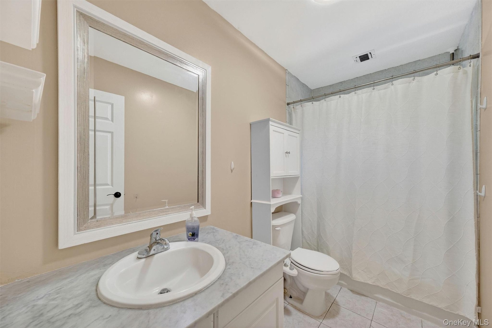 Vanity with an integrated oval sink, framed mirror, and a shower-tub combination with tile surround