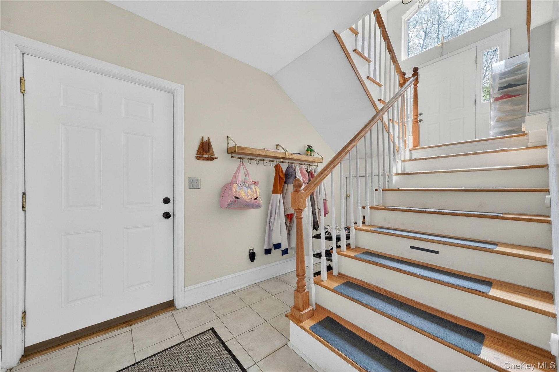 Two-story entry with a wood handrail, white balusters, tiled flooring, and a paneled entry door