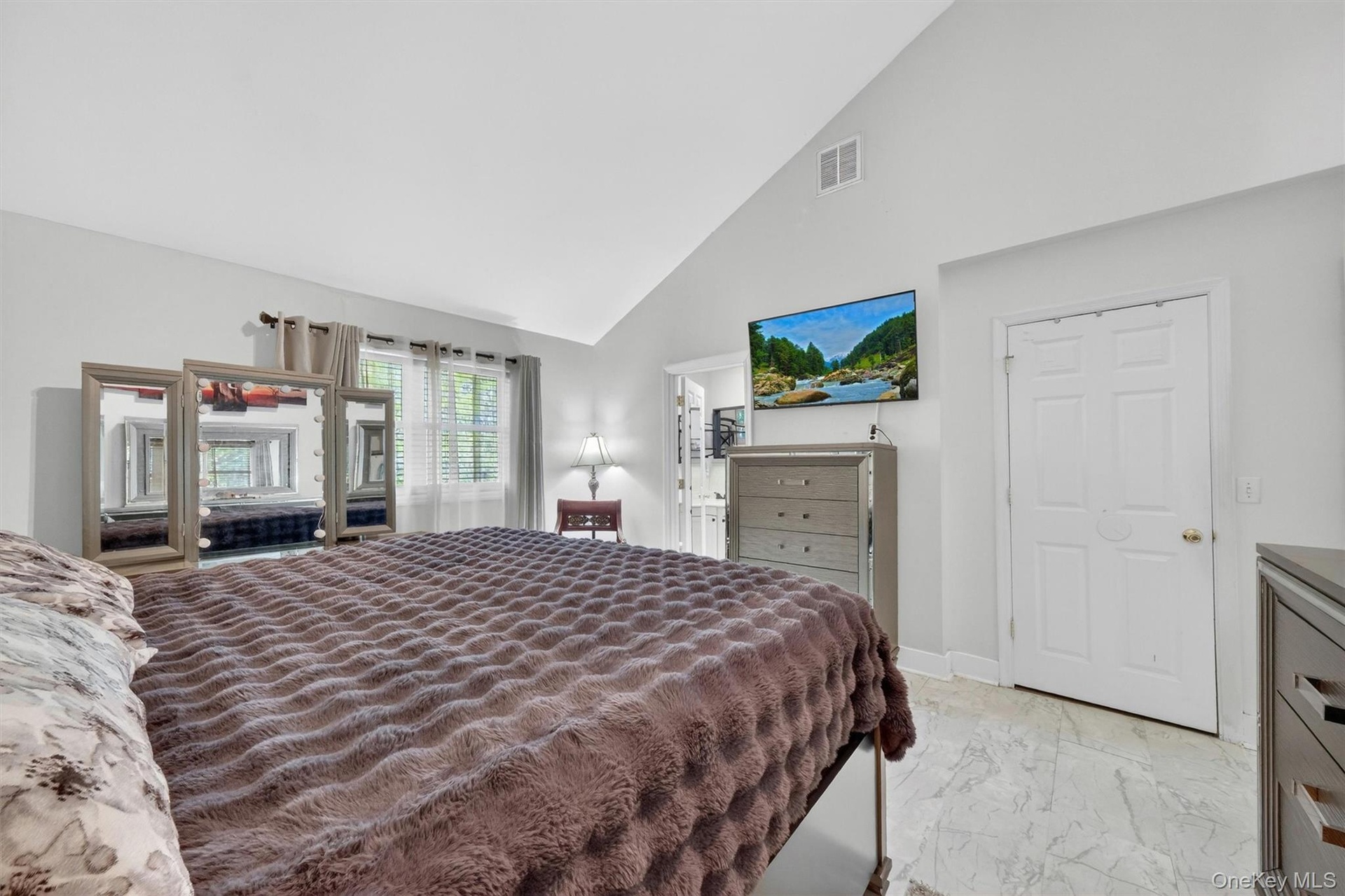Vaulted ceiling, white painted walls, window with blinds and curtains, white paneled door, and light-colored tile flooring
