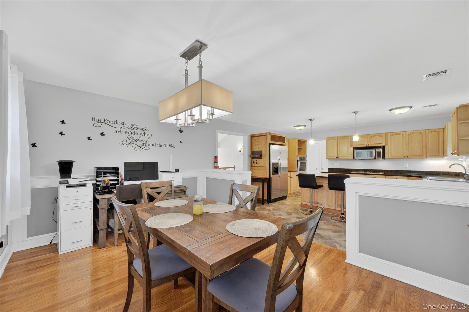 Open-concept living space featuring wood-finish flooring, a contemporary chandelier, and a kitchen with wood cabinetry, dark countertops, and stainles