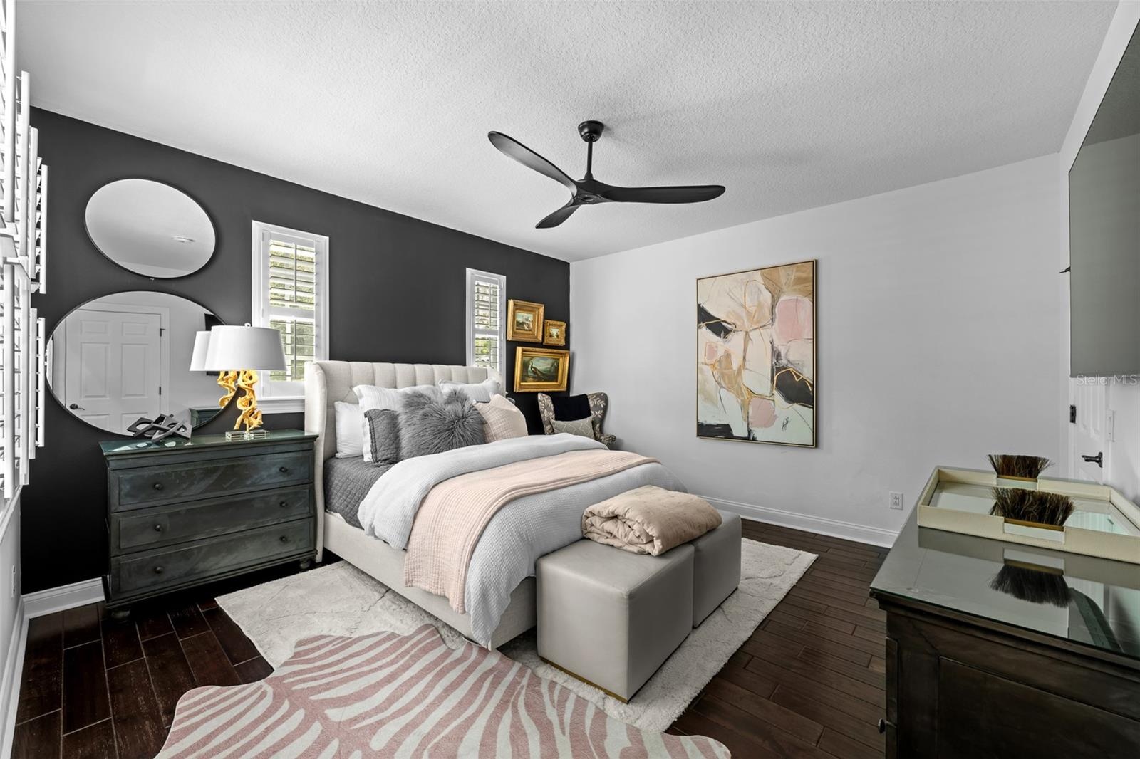 Dark wood flooring, accent wall, and windows with plantation shutters.