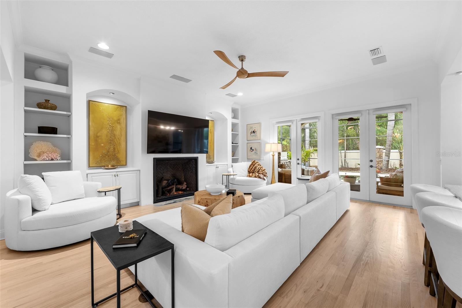 Built-in bookcases flanking the fireplace, French doors with lanai access, and light wood flooring.