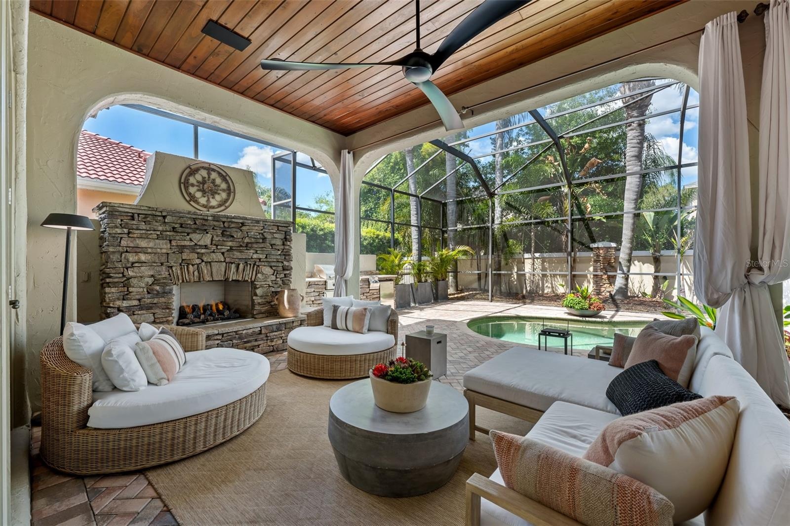 Lounge seating, stacked-stone fireplace, and arched openings to the pool.