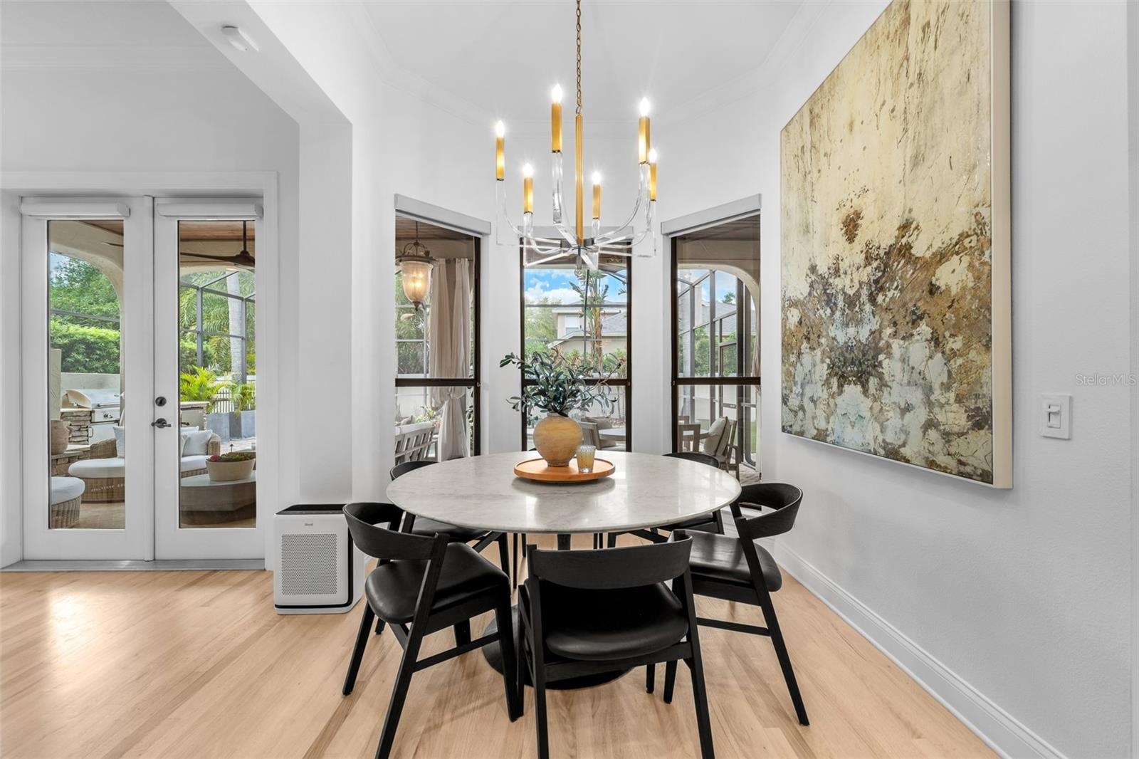 Casual dining area with French doors to the lanai, candle-style chandelier, and light wood flooring.