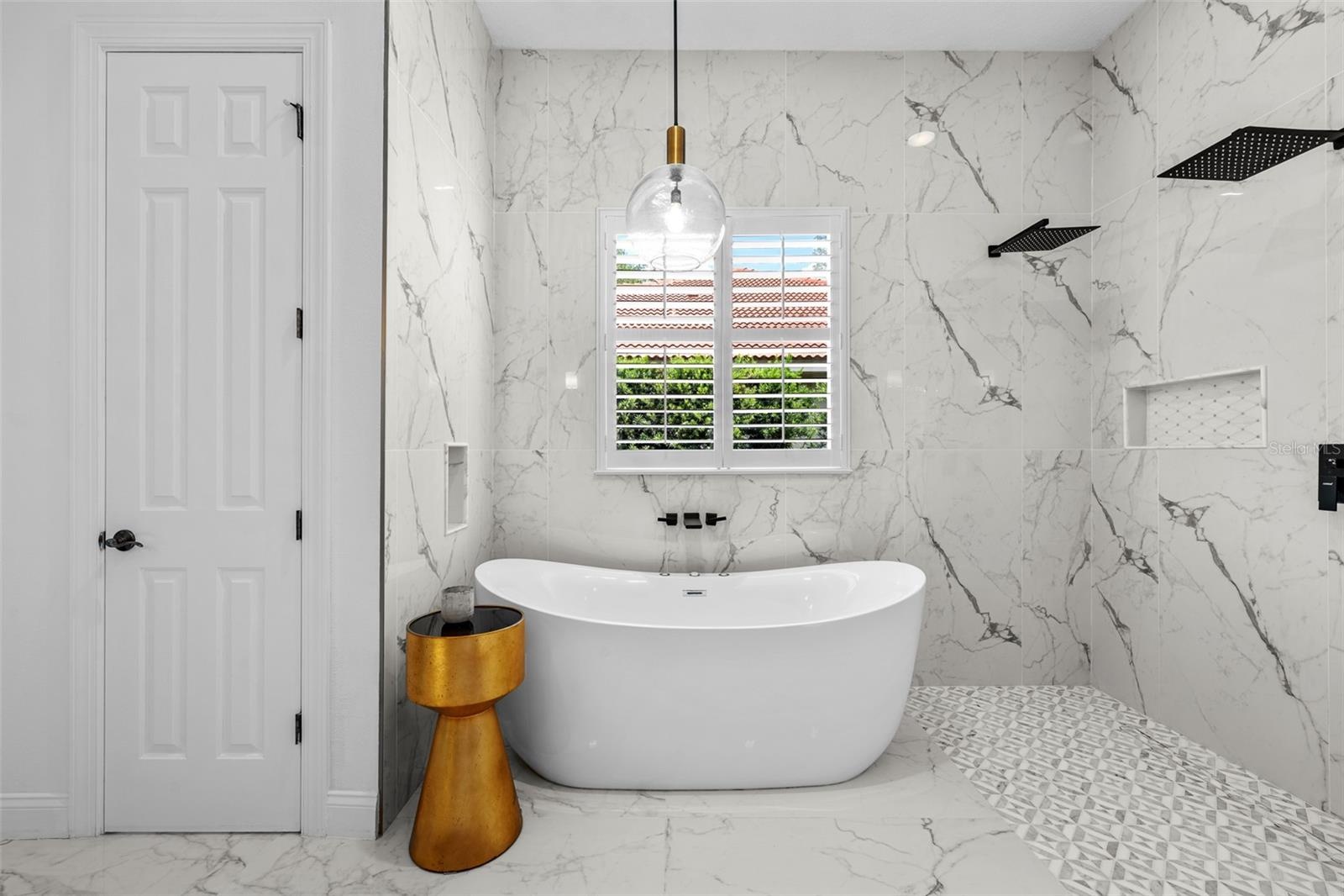 Freestanding tub inside the walk-in shower with window and plantation shutters.