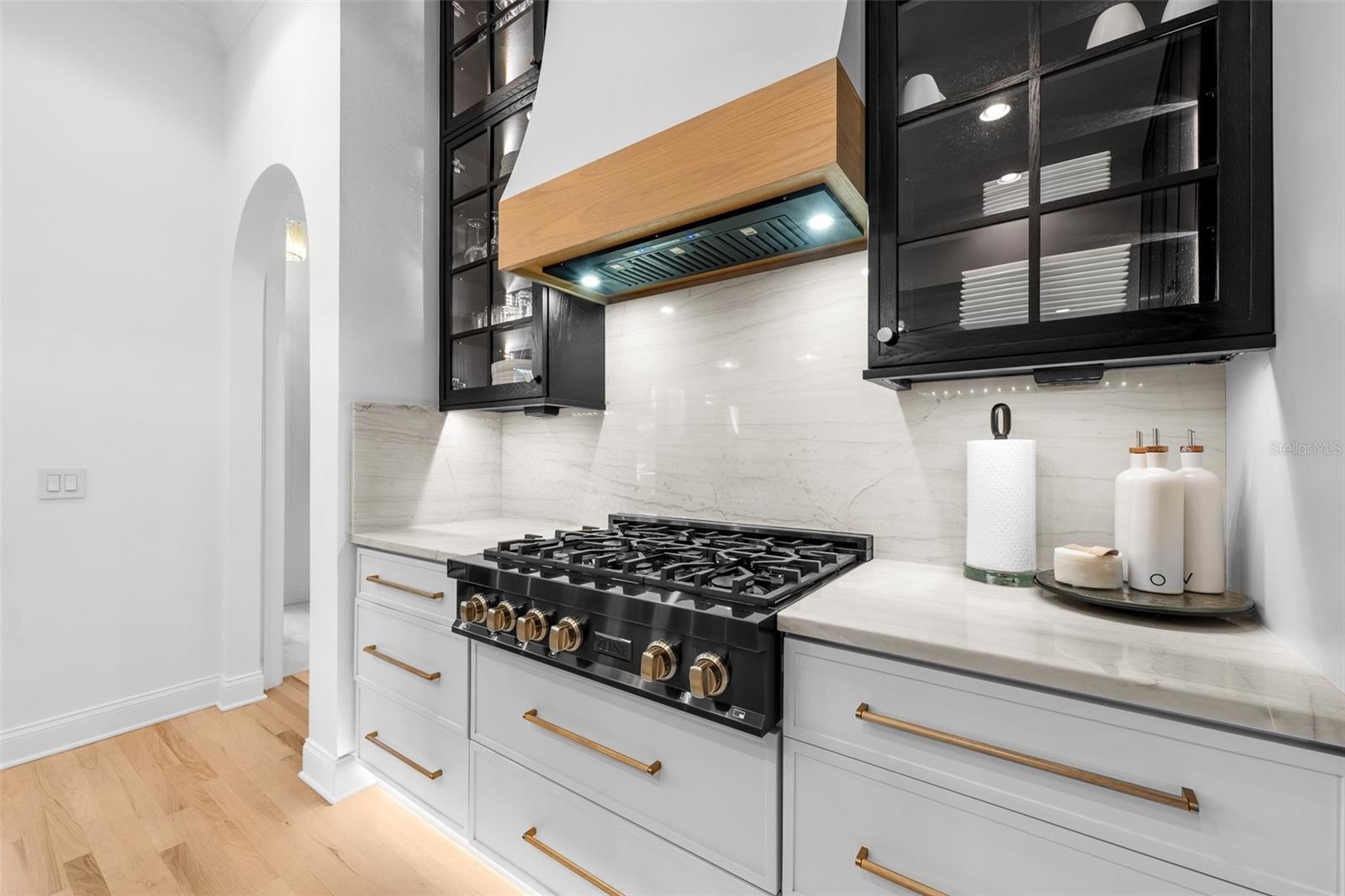 Six-burner gas cooktop, white tile backsplash, brass cabinet pulls, and stone countertops.