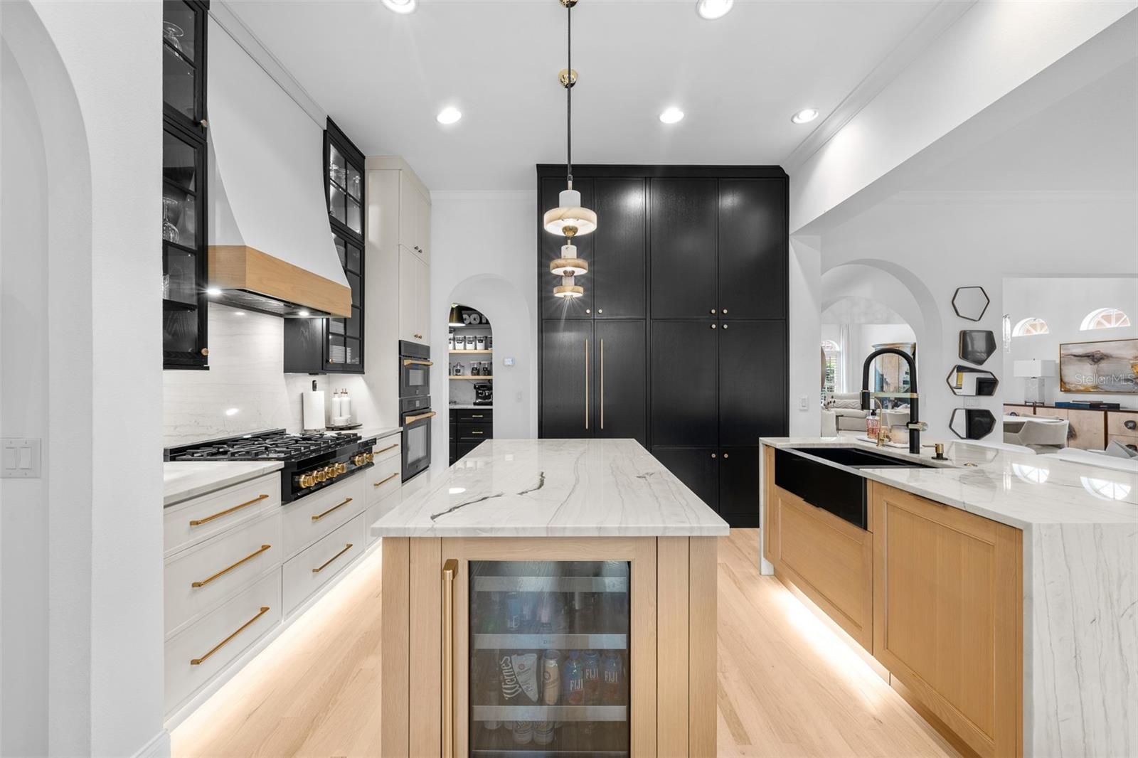 Island with built-in wine refrigerator, black pantry cabinetry, and glass-front uppers with pendant lighting.