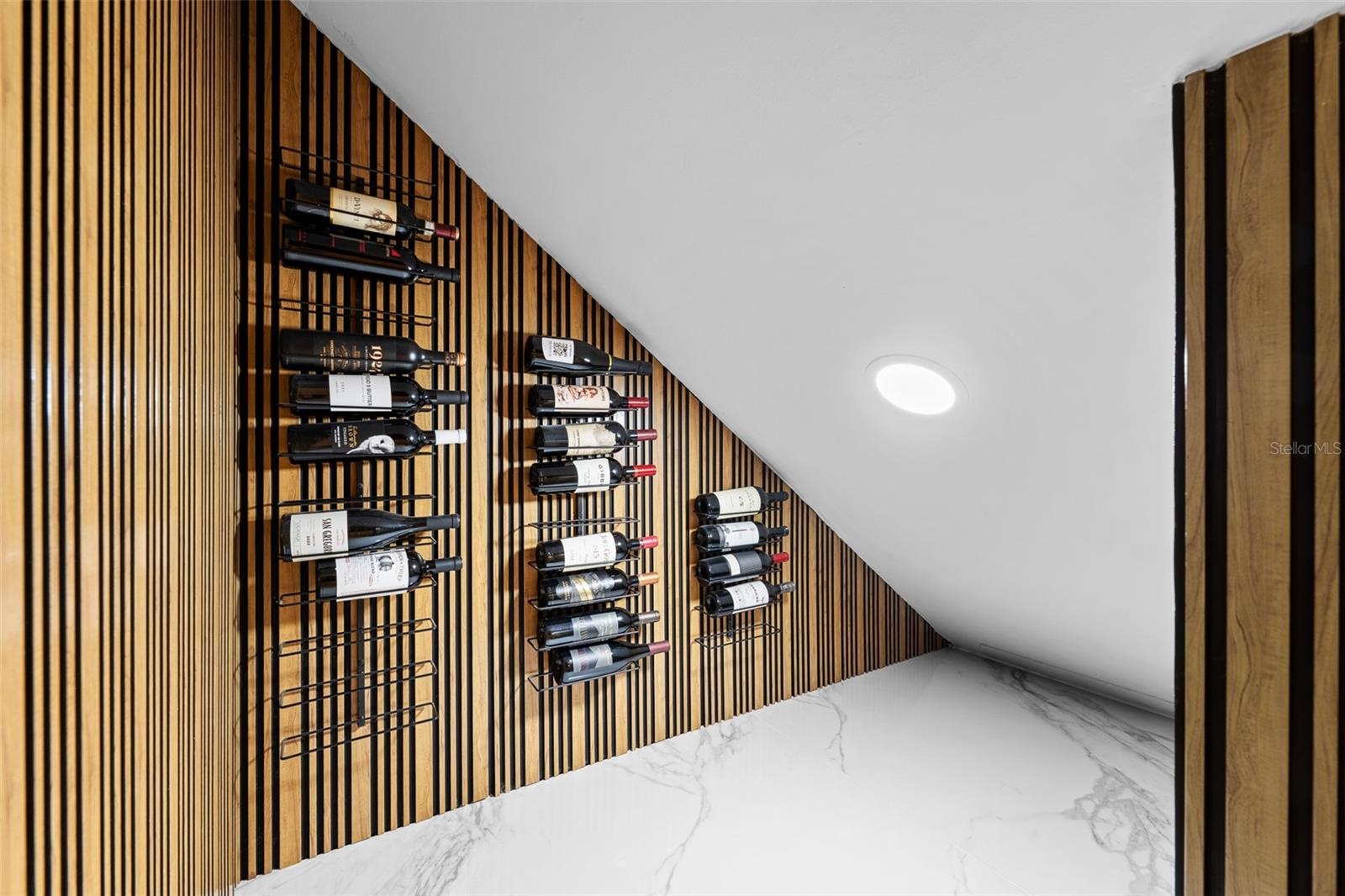 Wall-mounted wine racks on a vertical wood slat wall with recessed lighting.