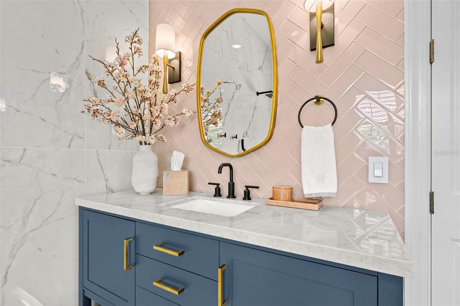 Vanity detail with brass-framed mirror, sconces, and matte black faucet.