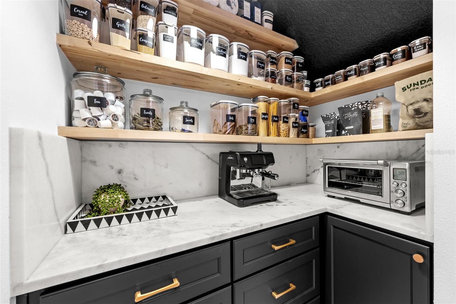 Floating wood shelving, stone counters, and black lower cabinets with brass hardware.