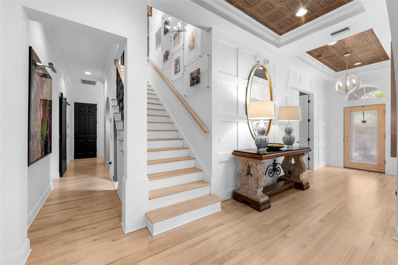 Wood-tread stairs with iron spindles, wall paneling, and a wood-inlay tray ceiling above the entry.