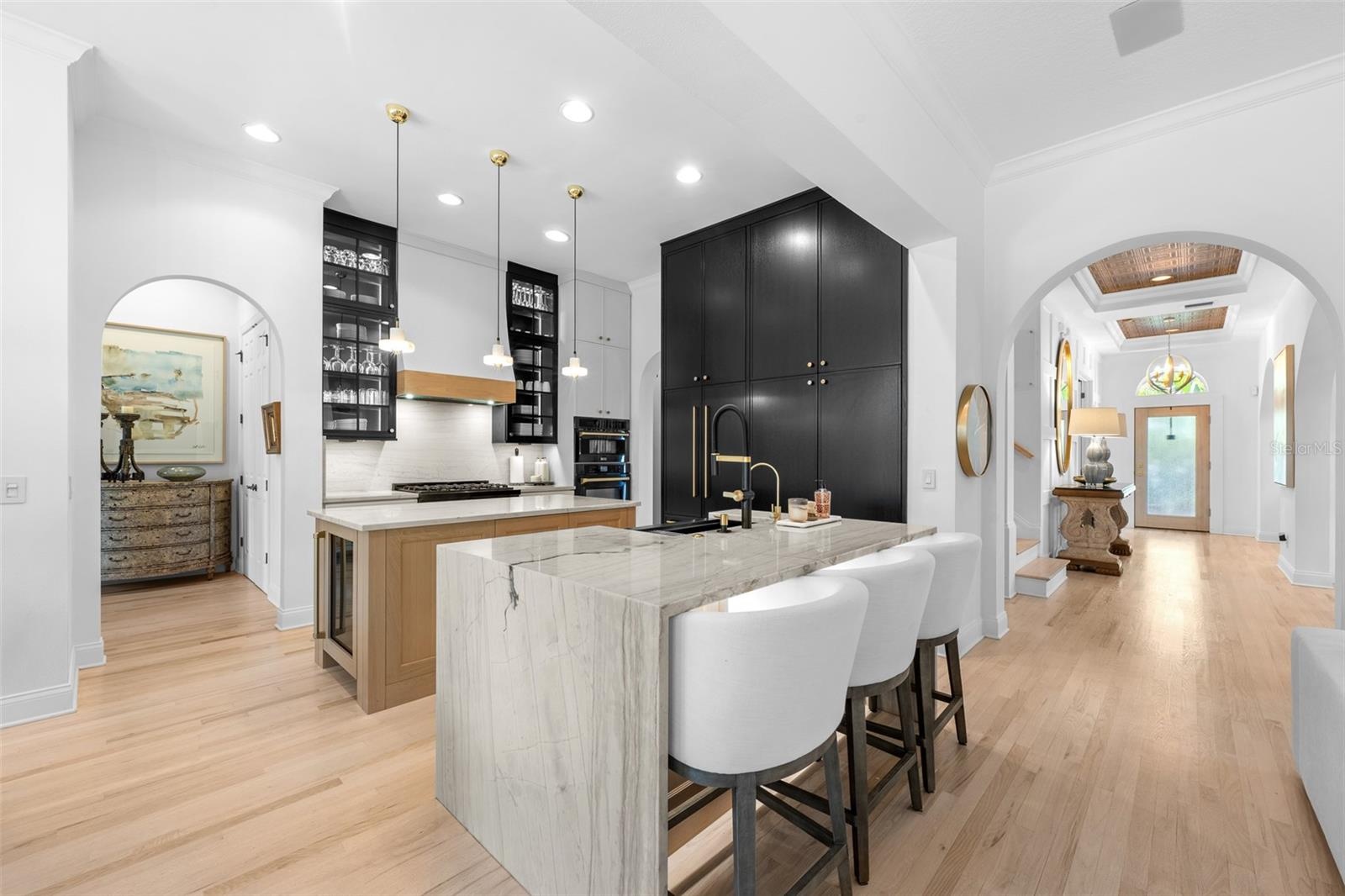 Two-tone cabinetry, waterfall-edge stone island with bar seating, pendant lighting, and arched openings to the foyer.
