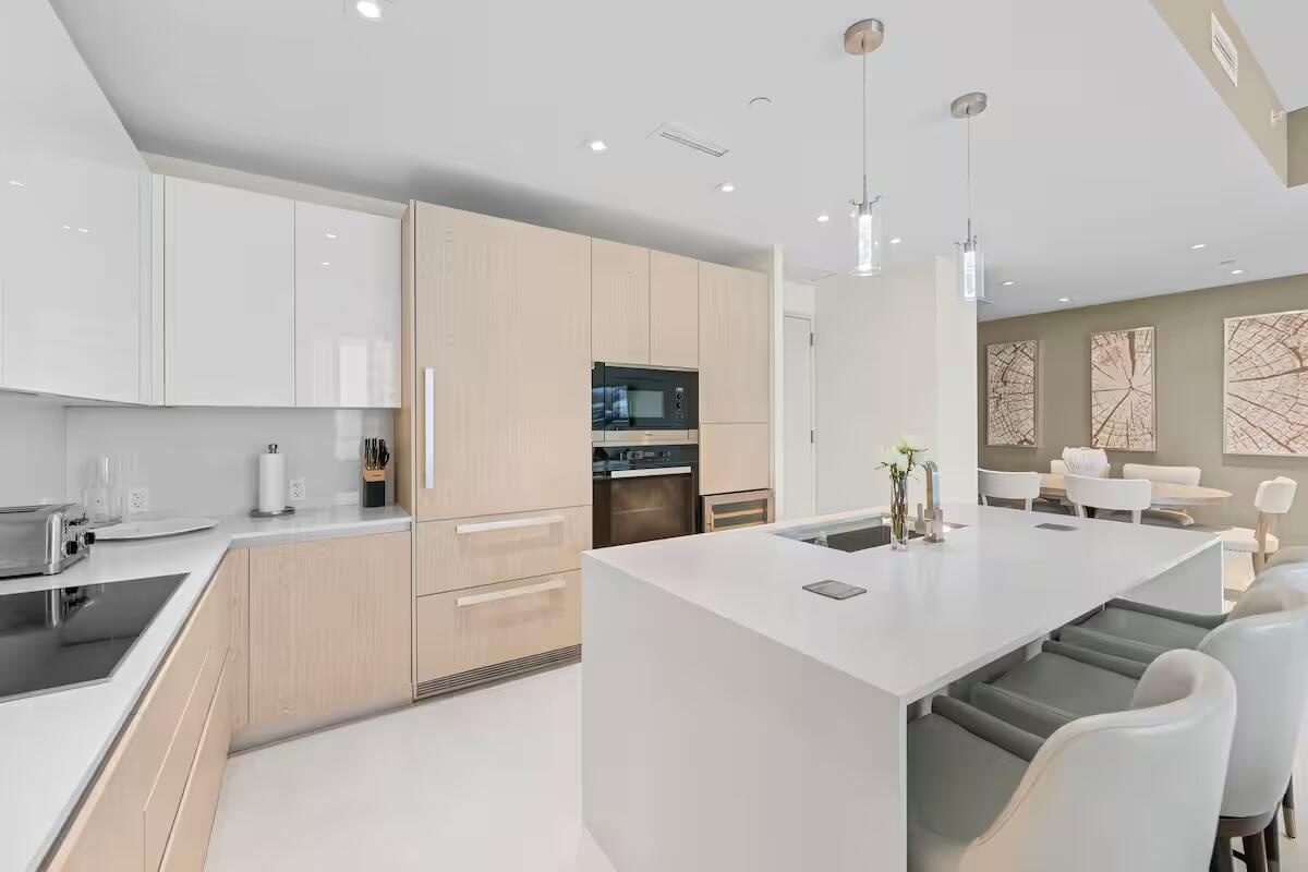 Sleek kitchen featuring a large island with integrated sink, contemporary recessed lighting, light wood-finish cabinetry, built-in oven, and a flat-su