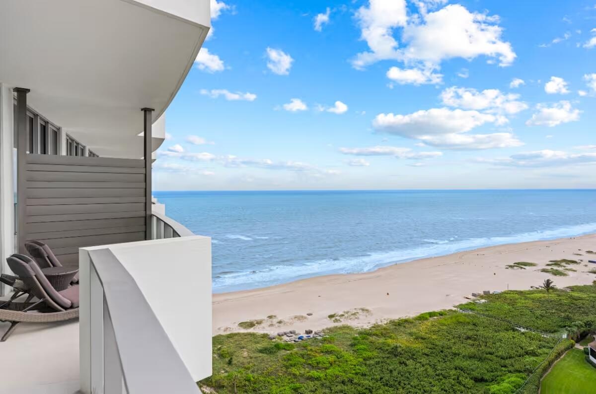 Private balcony with a curved design, featuring a partial privacy screen, and an expansive ocean and beach horizon