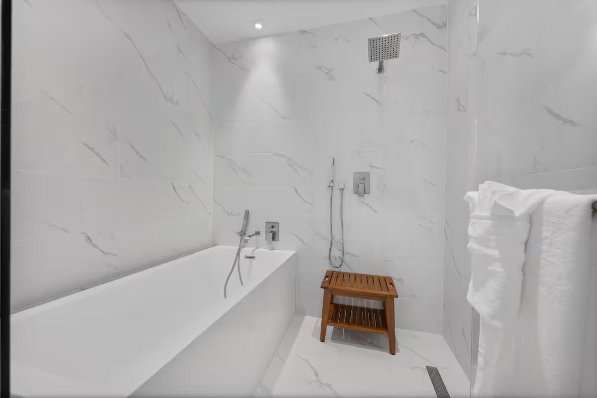 Freestanding soaking tub with a wall-mounted faucet, complemented by a rainfall shower head and white veined tile