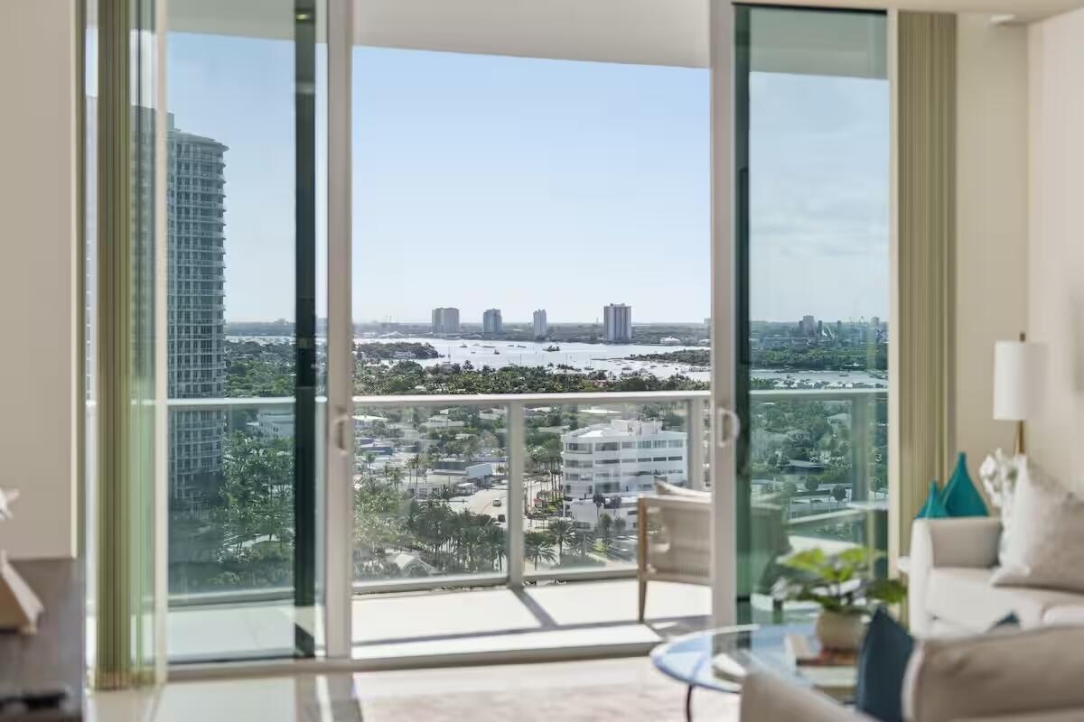 Sliding glass doors opening to a private balcony with glass railings, showcasing expansive water and city vistas