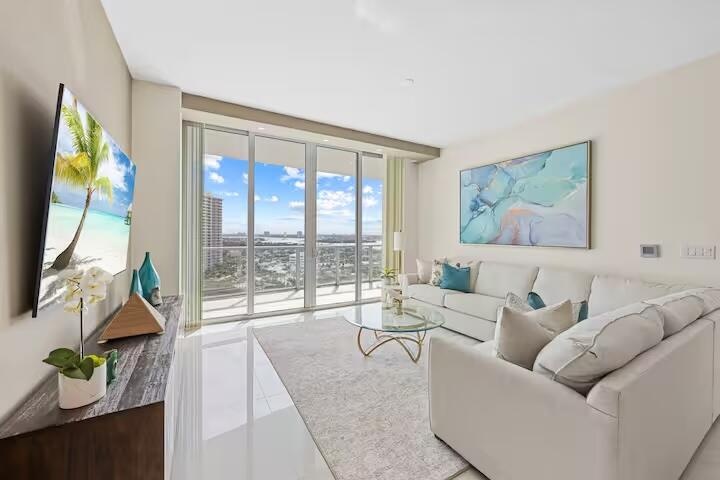 Expansive floor-to-ceiling windows, high ceilings, a wall-mounted television, polished tile flooring, and a built-in credenza