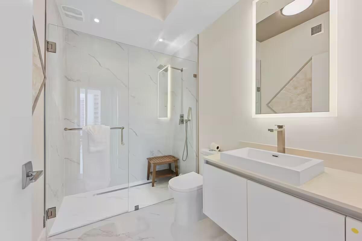 Glass-enclosed shower with full-height tile surround, illuminated vanity mirror, and a rectangular vessel sink with a single-handle faucet