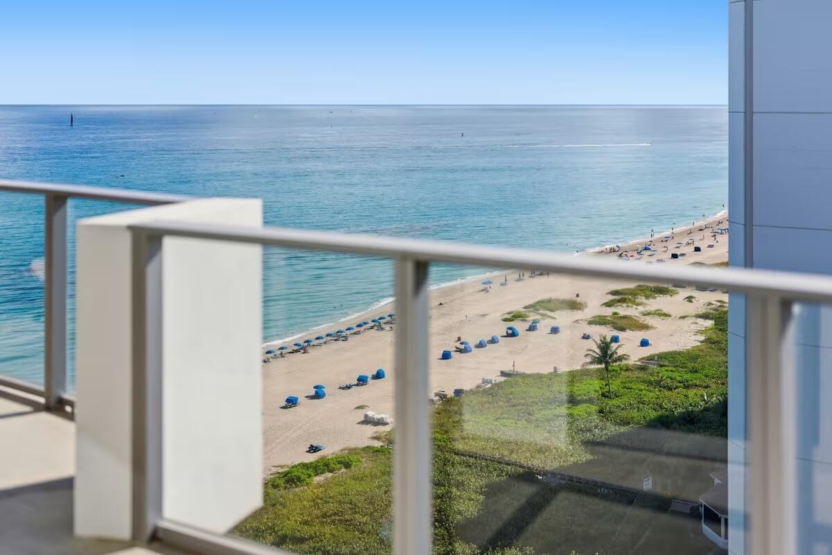 Balcony with glass panel railing and aluminum frame, overlooking the ocean and sandy beach
