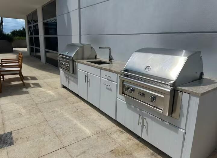 Outdoor kitchen featuring a built-in grill, integrated sink, and white cabinetry with stone countertops