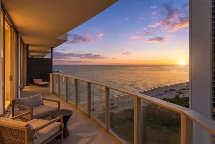 Expansive balcony with glass railings and concrete flooring, featuring ocean and beach scenery