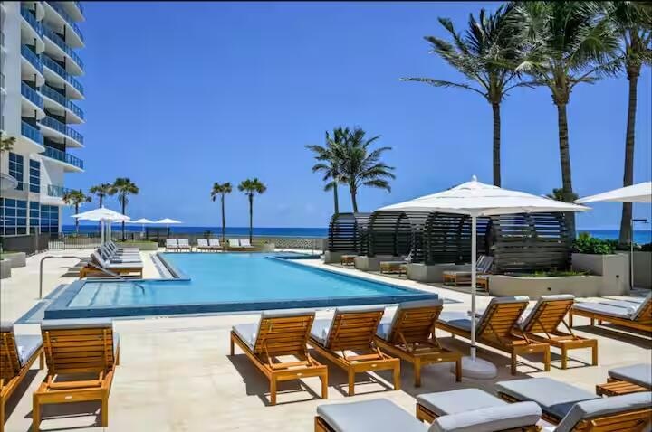 Resort-style pool area featuring multiple chaise lounges, structured cabanas, and ocean scenery