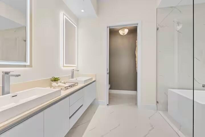 Dual vessel sinks with wall-mounted lighting, extensive vanity storage, and a glass-enclosed shower featuring a built-in tub