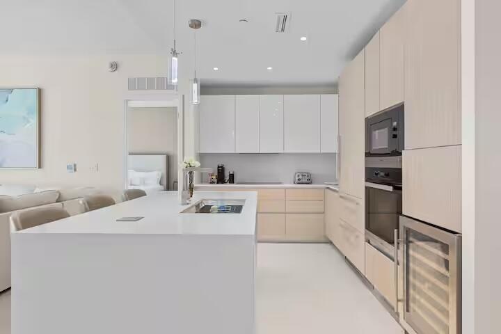 Modern kitchen featuring a waterfall island, integrated sink, pendant lighting, and stainless steel appliances