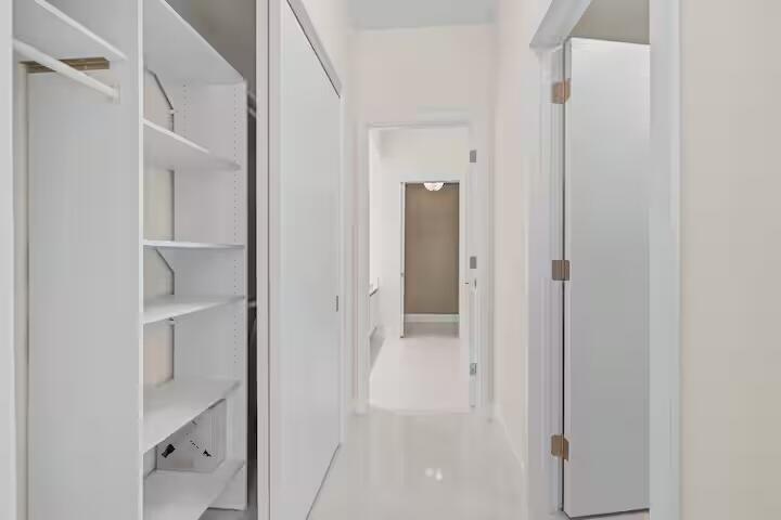 Hallway featuring white walls, light-toned flooring, built-in shelving, and a closet with a hanging rod